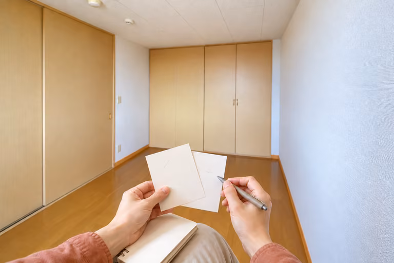 木製収納のある室内で、二枚のメモを見比べる手元