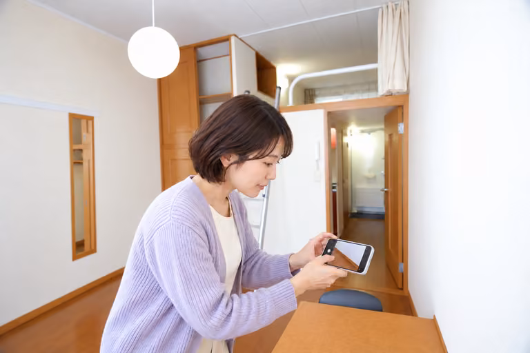 室内の壁と床の境目をスマートフォンで記録する女性の横顔