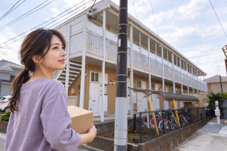 小さな段ボール箱を抱え、建物の前に立つ女性の自然な横顔