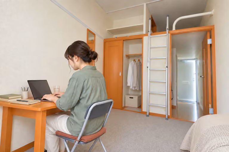 本や筆記具を置いた机で、パソコンに向かう女性
