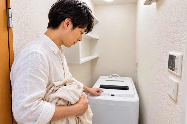 洗濯物を手に、備え付けの洗濯機を確認する男性の横顔