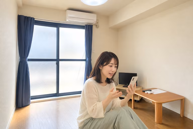 窓とローテーブルのある室内で、スマートフォンを使う女性の横顔