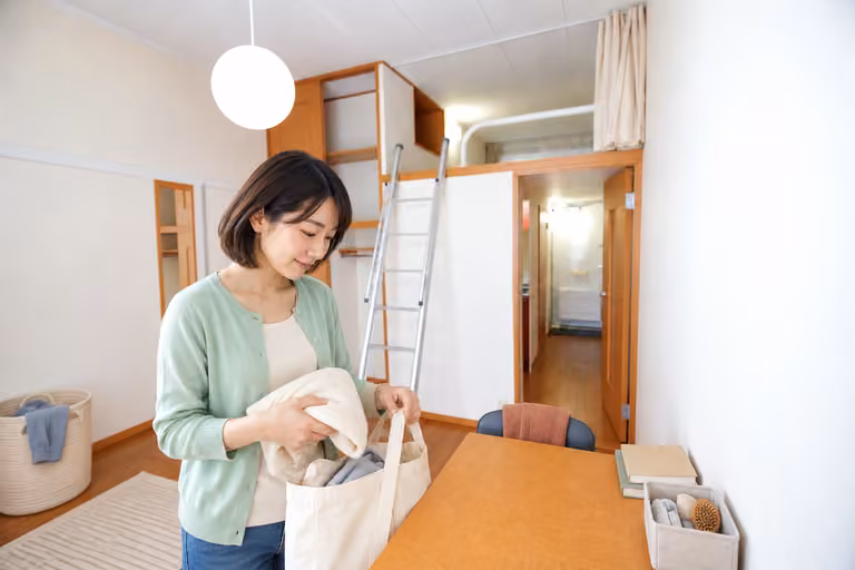 収納かごや本を置いた部屋で、衣類とバッグを整理する女性