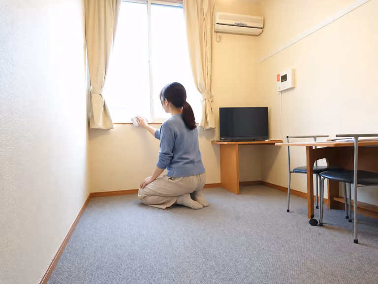 レオパレスの室内の床に膝をつき、窓の下部を布で拭く女性