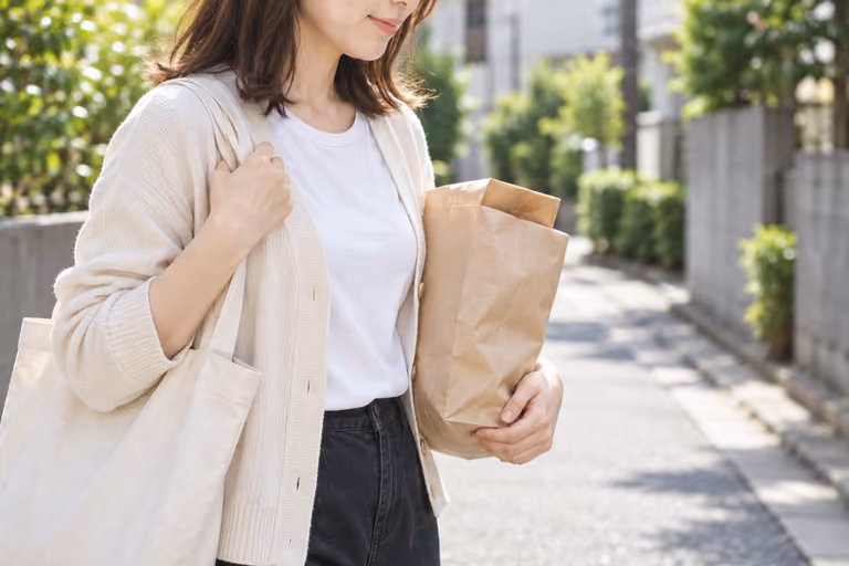 買い物の紙袋を持って住宅街を歩く女性の腕と上半身