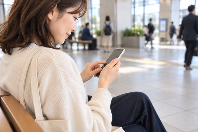 駅の待合スペースでスマートフォンを確認する手元