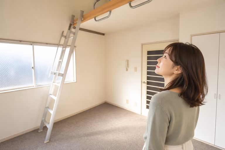 部屋の床に立ちロフトとはしごを見上げる女性の後ろ姿