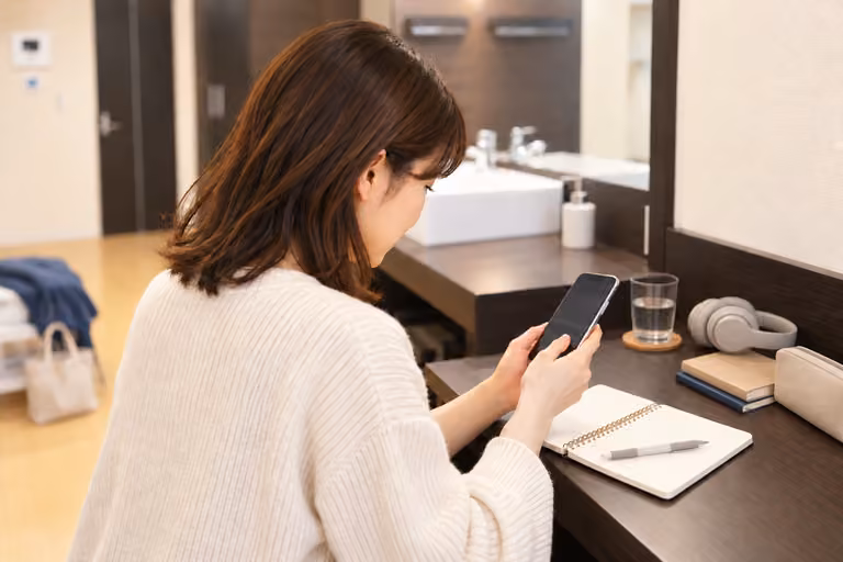 本やヘッドホンを置いたカウンターで、スマートフォンを見る女性