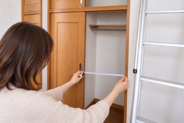 収納の開口部の両端にメジャーを当て、幅を確かめる女性の手元
